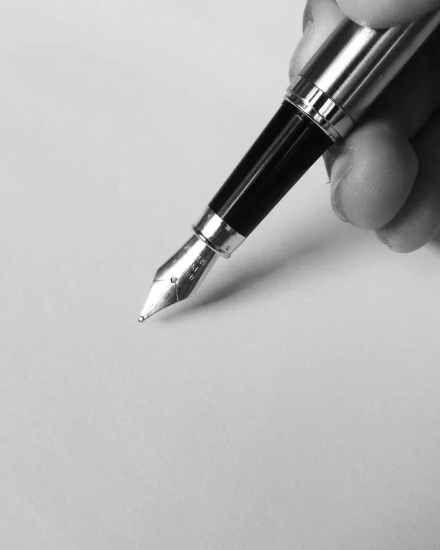 Une main tient un stylo plume au-dessus d’une feuille vierge.