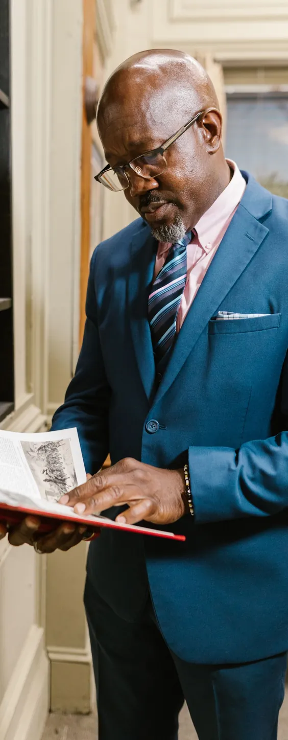 Un homme en costume, debout, lit un livre ouvert.